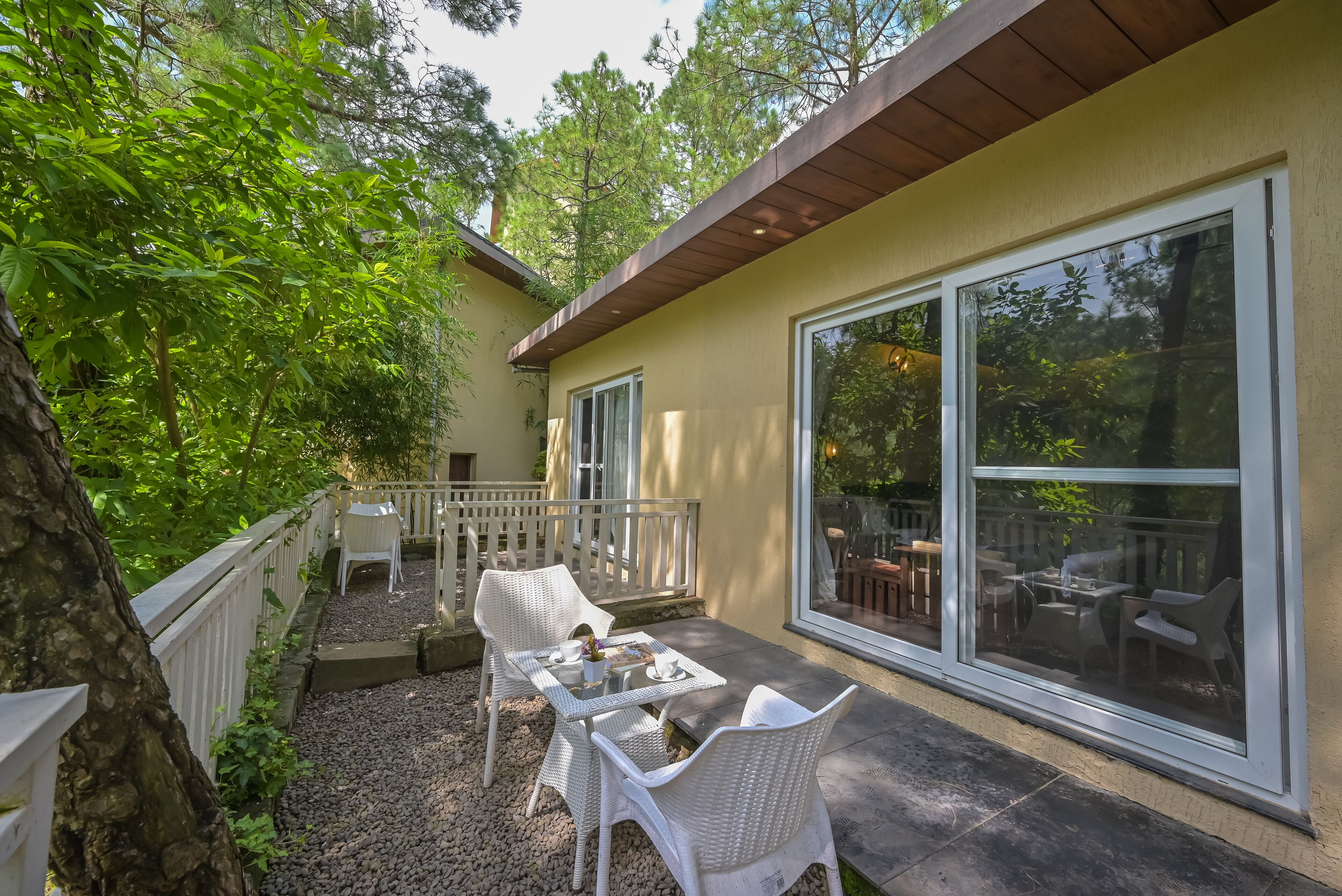 An outdoor patio with a table and chairs, surrounded by a white fence and trees.