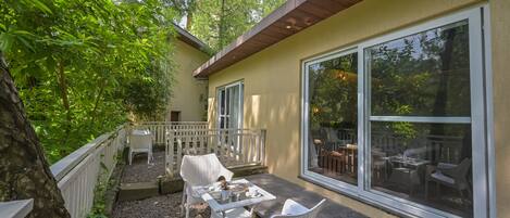 An outdoor patio with a table and chairs, surrounded by a white fence and trees.