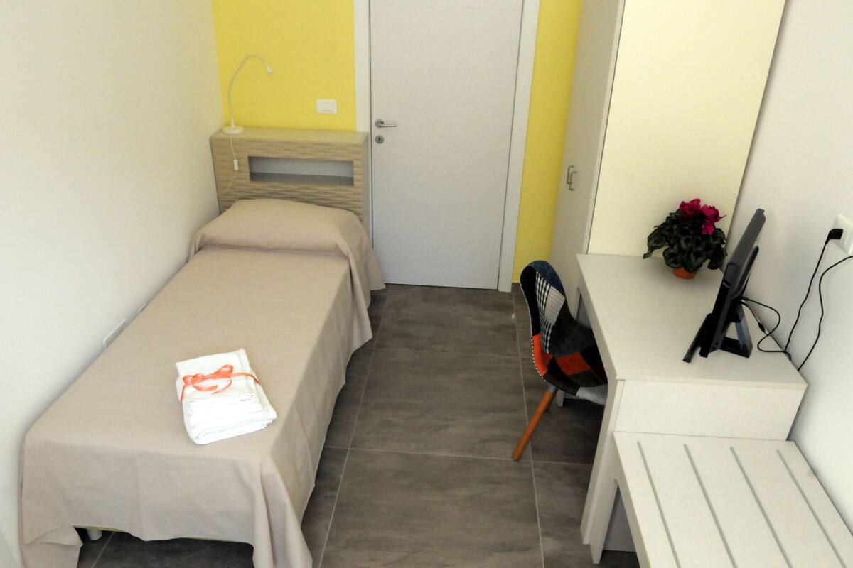 A small, neatly arranged room with a bed, a desk, and a chair.