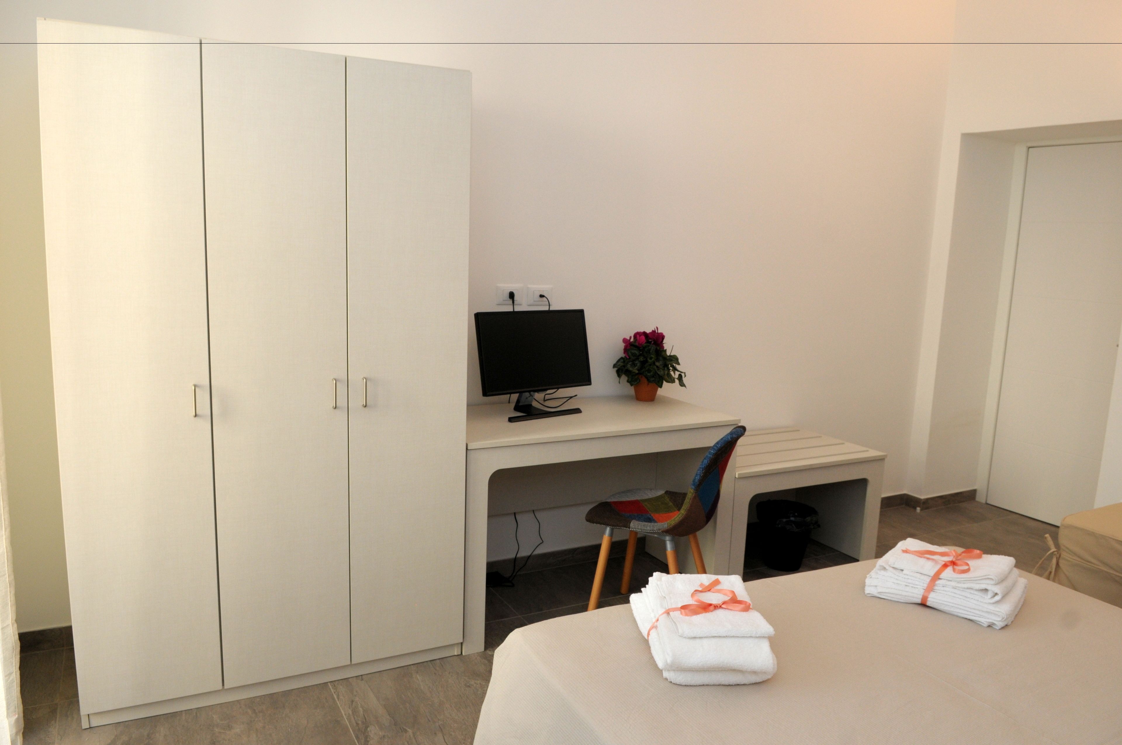 Et hotelværelse med en seng, et skrivebord med en computer, en stol, en potteplante og et klædeskab.