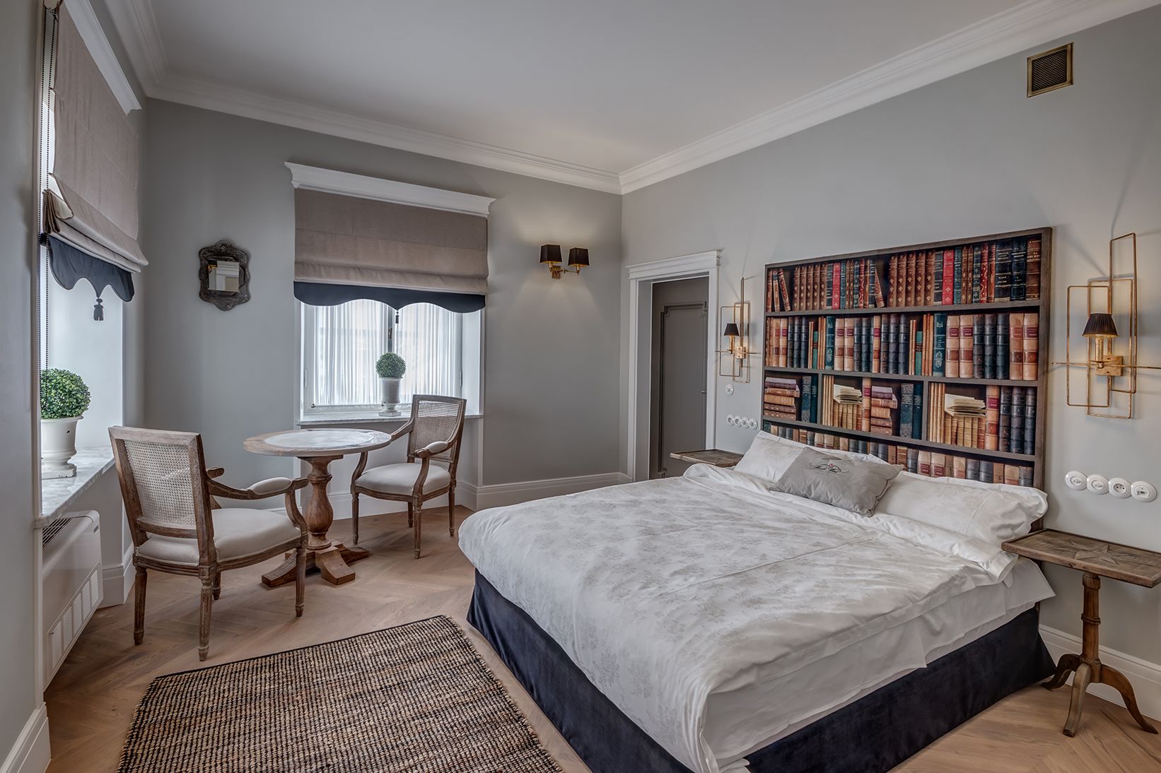 Une chambre à coucher avec un grand lit, une bibliothèque, une table à manger avec des chaises et une fenêtre avec des rideaux.