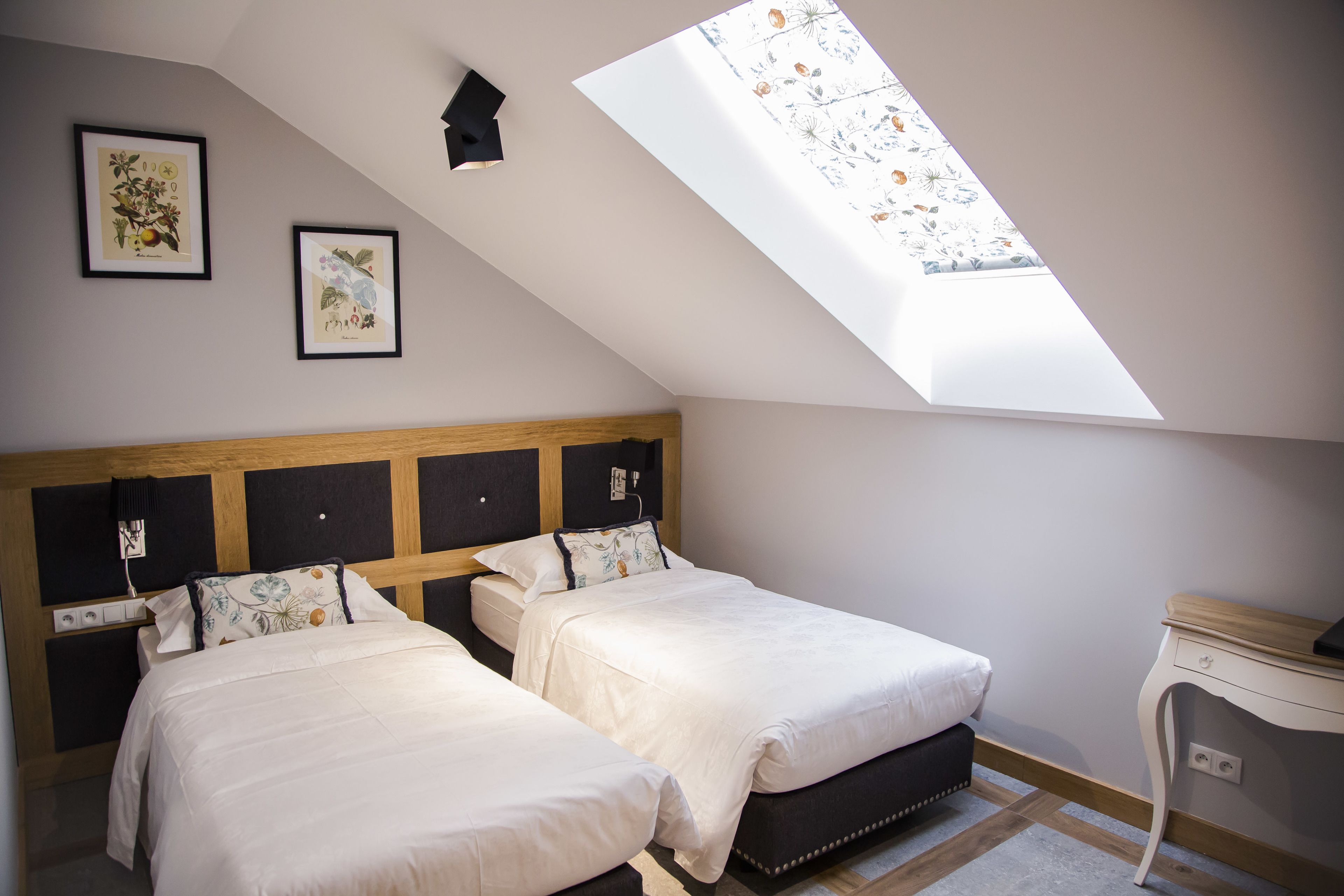 A bedroom with two beds, a skylight, and artwork on the wall.