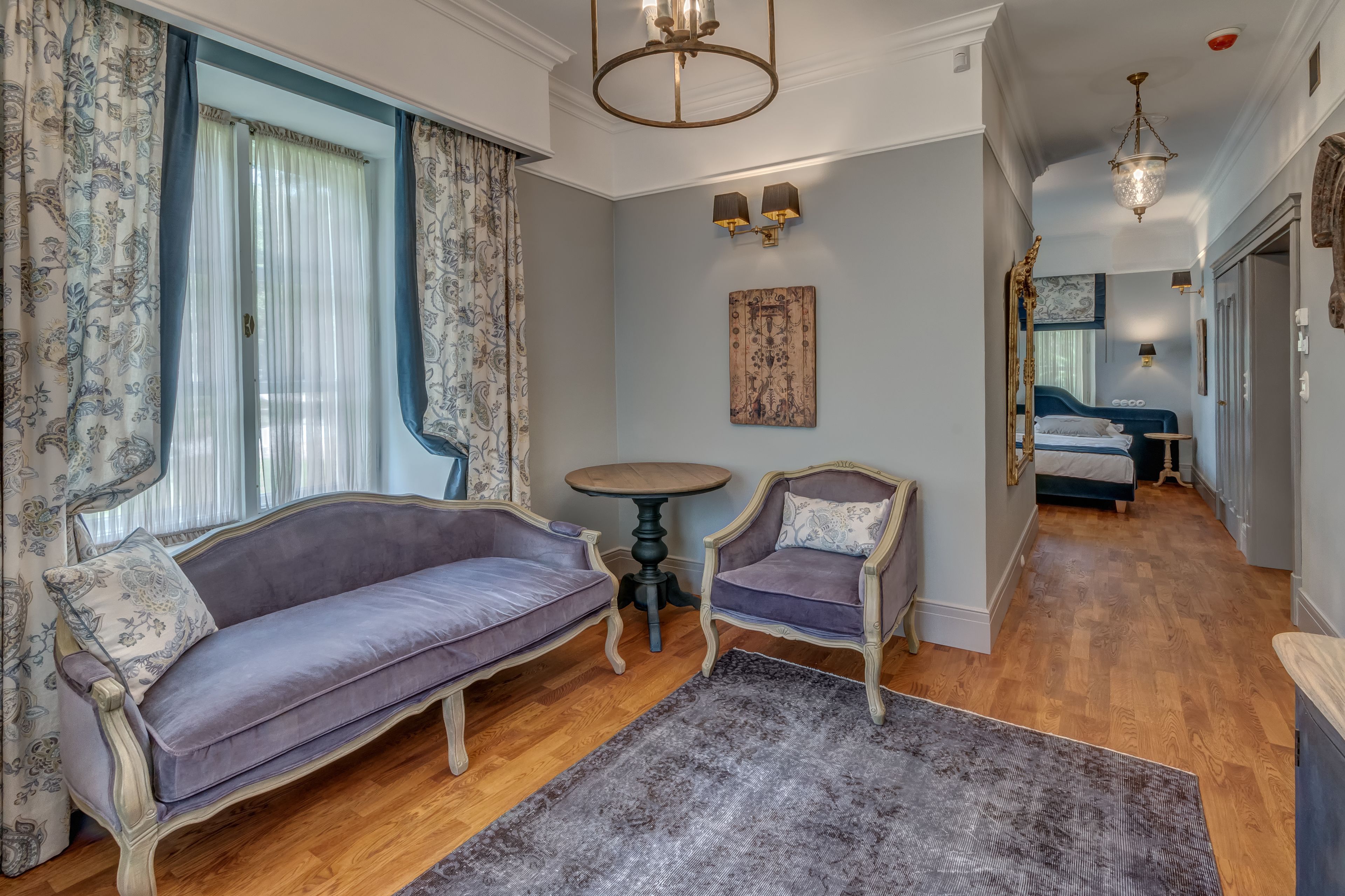 Ein Zimmer mit einem violetten Sofa, zwei Sesseln, einem kleinen runden Tisch und einem gemusterten Teppich.