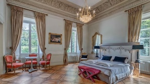 A spacious bedroom with a large bed, a sitting area with chairs, and a view of greenery through the windows. - Palac Mala Wies (Belsk Duzy)