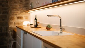 A kitchen with a wooden countertop, a white sink, and a stainless steel faucet. There is a bottle of wine and a small plant on the counter.