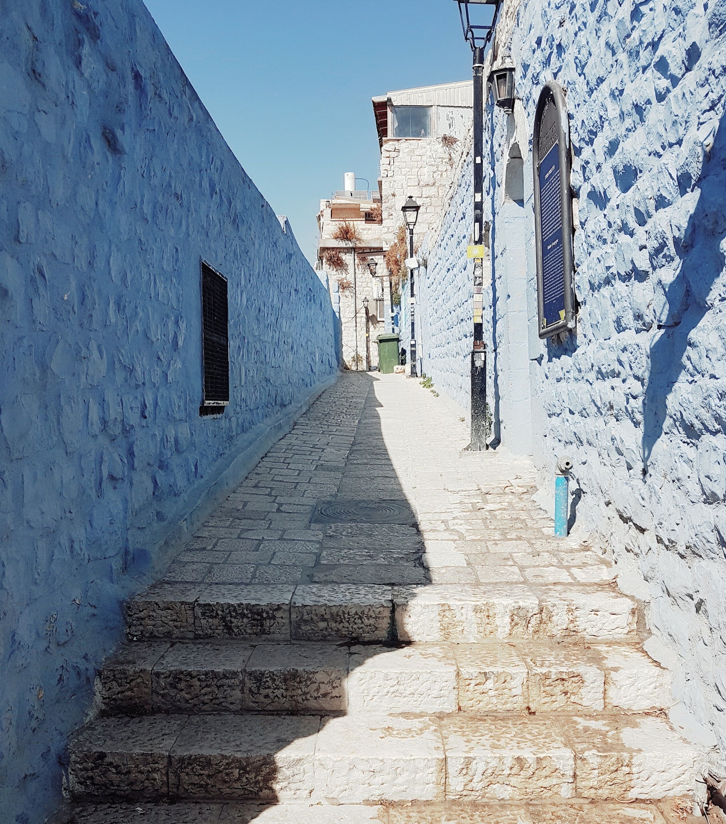 A narrow cobblestone street flanked by buildings with blue and white walls.