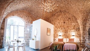 A room with a stone ceiling, a dining area with a table and chairs, a bed with two pillows, and a small plant on a side table.
