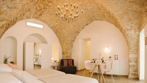 A bedroom with a stone ceiling, a chandelier, a bed with white linens, and a dining area with a table and chairs.