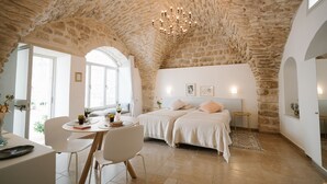 A room with a stone ceiling, two beds, a dining area, and a chandelier.