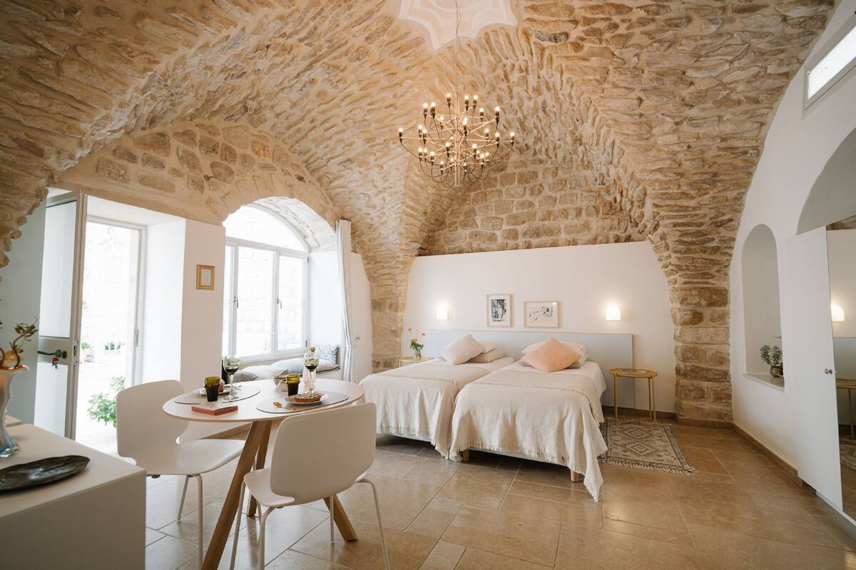 A room with a stone ceiling, two beds, a dining area, and a chandelier.