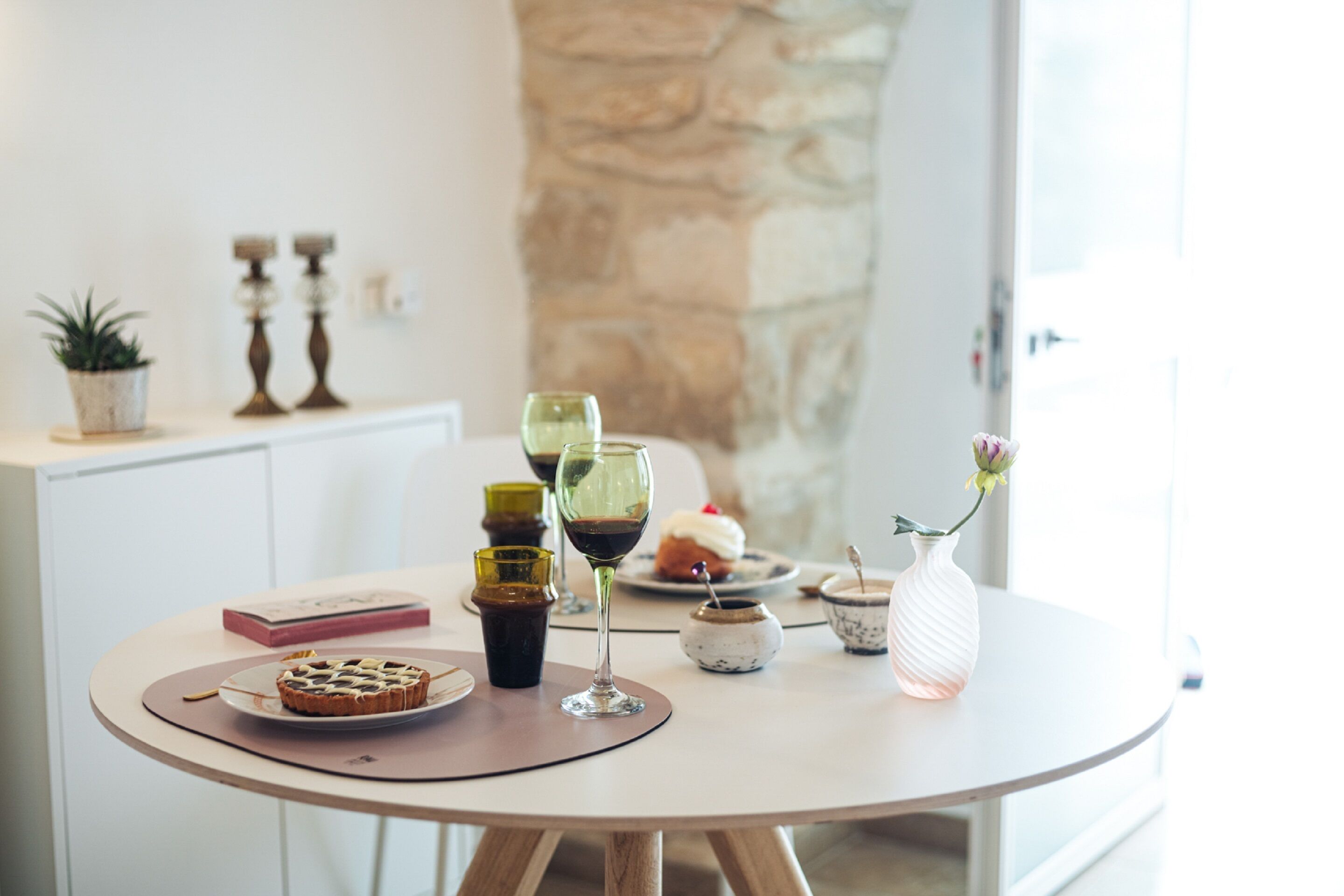 A round table with a dessert, a glass of red wine, and a vase with flowers.