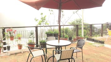 A patio with a round table and four chairs, surrounded by potted plants and a red umbrella.