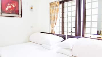A neatly made bed with white linens and pillows, a window with curtains, and a framed artwork on the wall.
