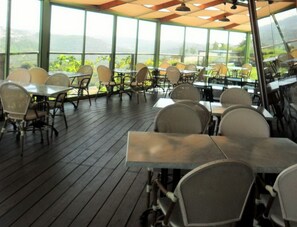 An outdoor dining area with tables and chairs, large windows, and a view of the landscape.