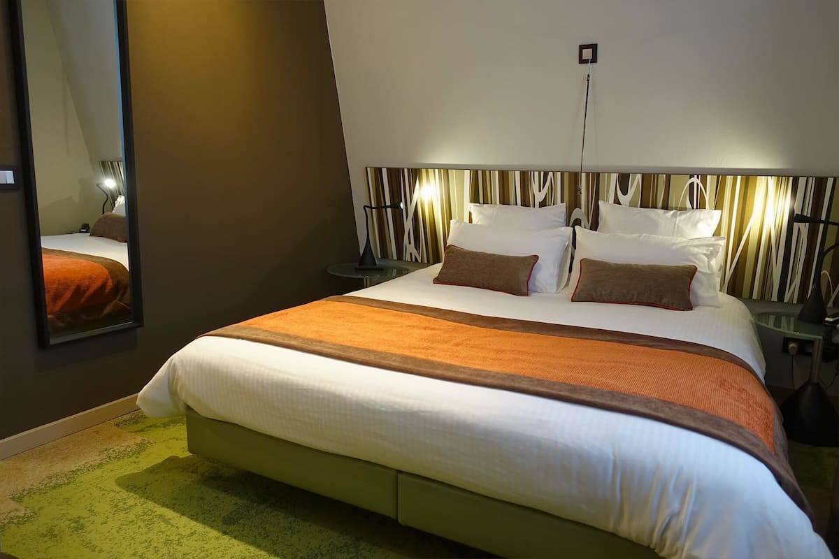 A neatly made bed with a white and brown bedspread, two pillows, and a nightstand with a lamp.