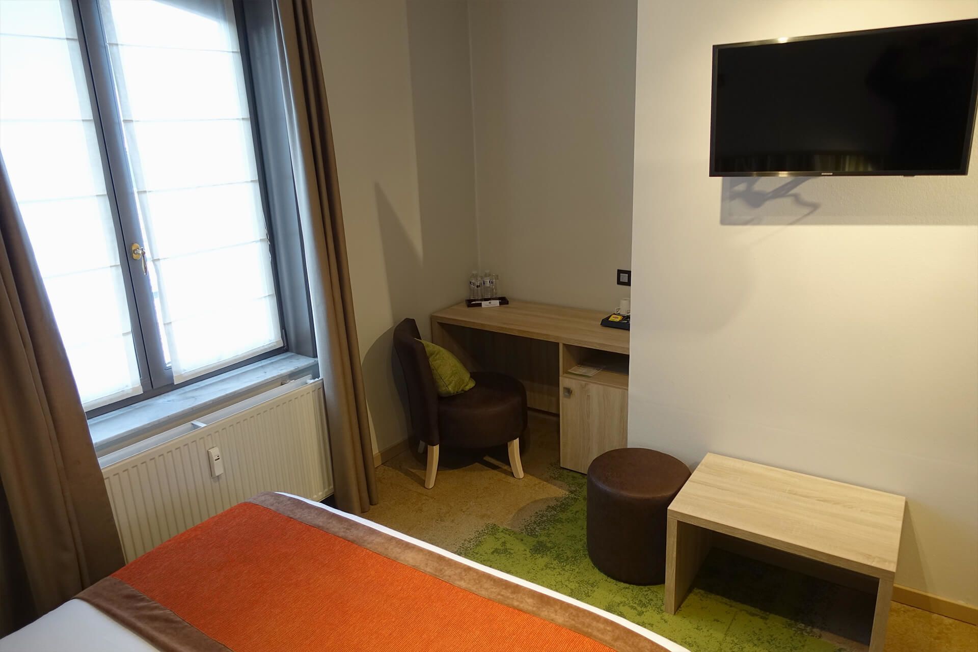 Een hotelkamer met een bed, een bureau, een stoel, een televisie en een raam met gordijnen.