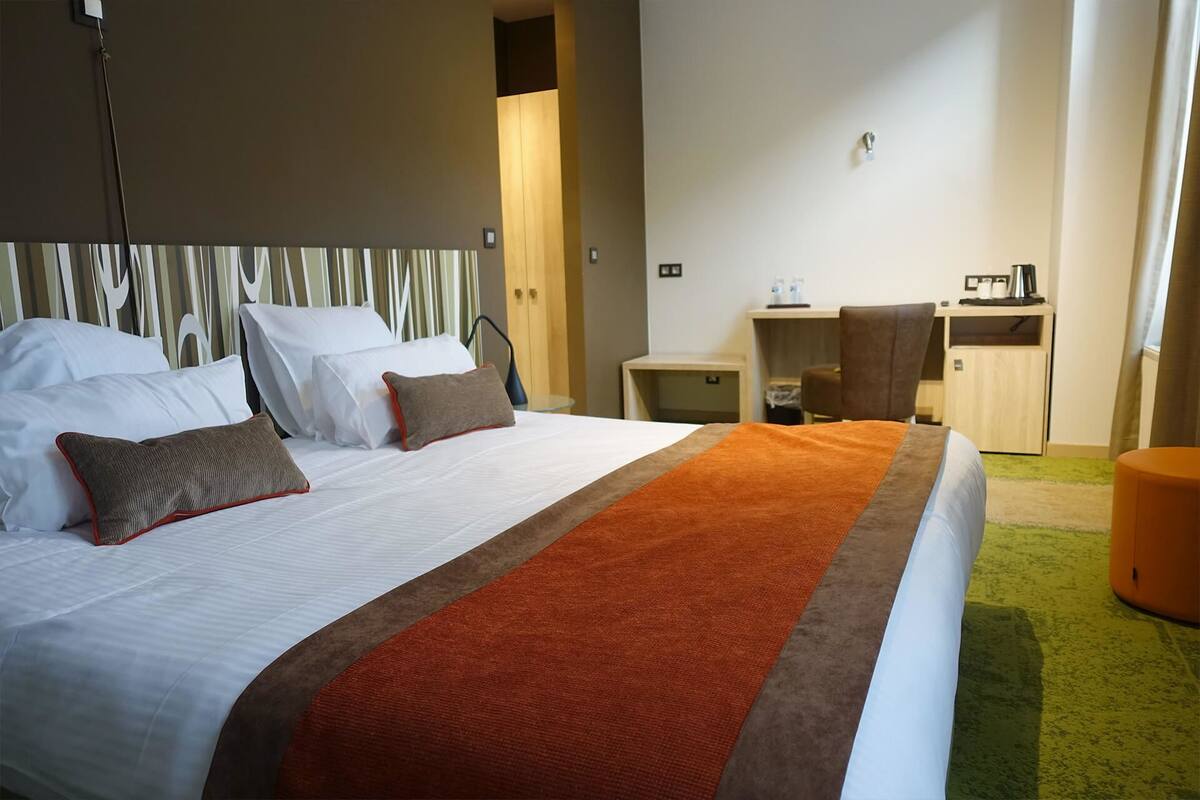 A hotel room with a large bed, a desk, and a chair.