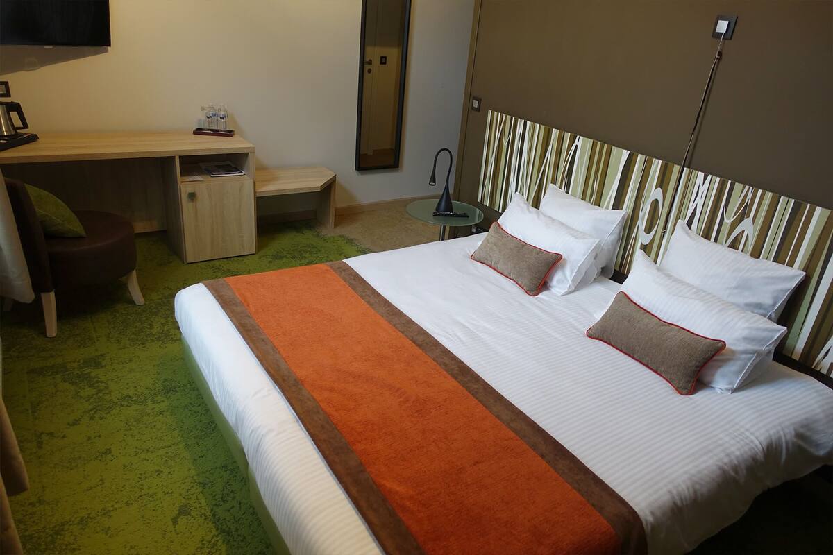 A hotel room with a bed, a desk, a chair, and a small table.