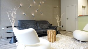 A modern living room with a black leather sofa, white chairs, a glass coffee table, and a decorative wall with lights. - Hôtel du Parc (Ath)