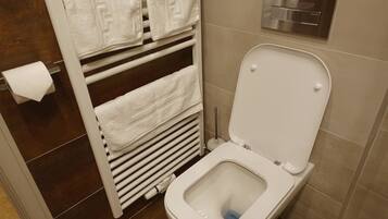 A modern bathroom with a white toilet, a towel rack with folded towels, a toilet paper holder, and a wall-mounted flush tank.