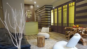 A modern hotel lobby with a reception desk, a seating area with sofas and chairs, a decorative wooden table, and a wall with striped patterns and a door with frosted glass panels. - Hôtel du Parc (Ath)