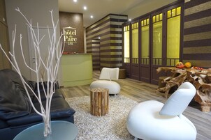 Un moderno vestíbulo de hotel con un mostrador de recepción, una zona de estar con sofás y sillones, una mesa de madera decorativa y una pared con diseños a rayas y una puerta con paneles de vidrio esmerilado.