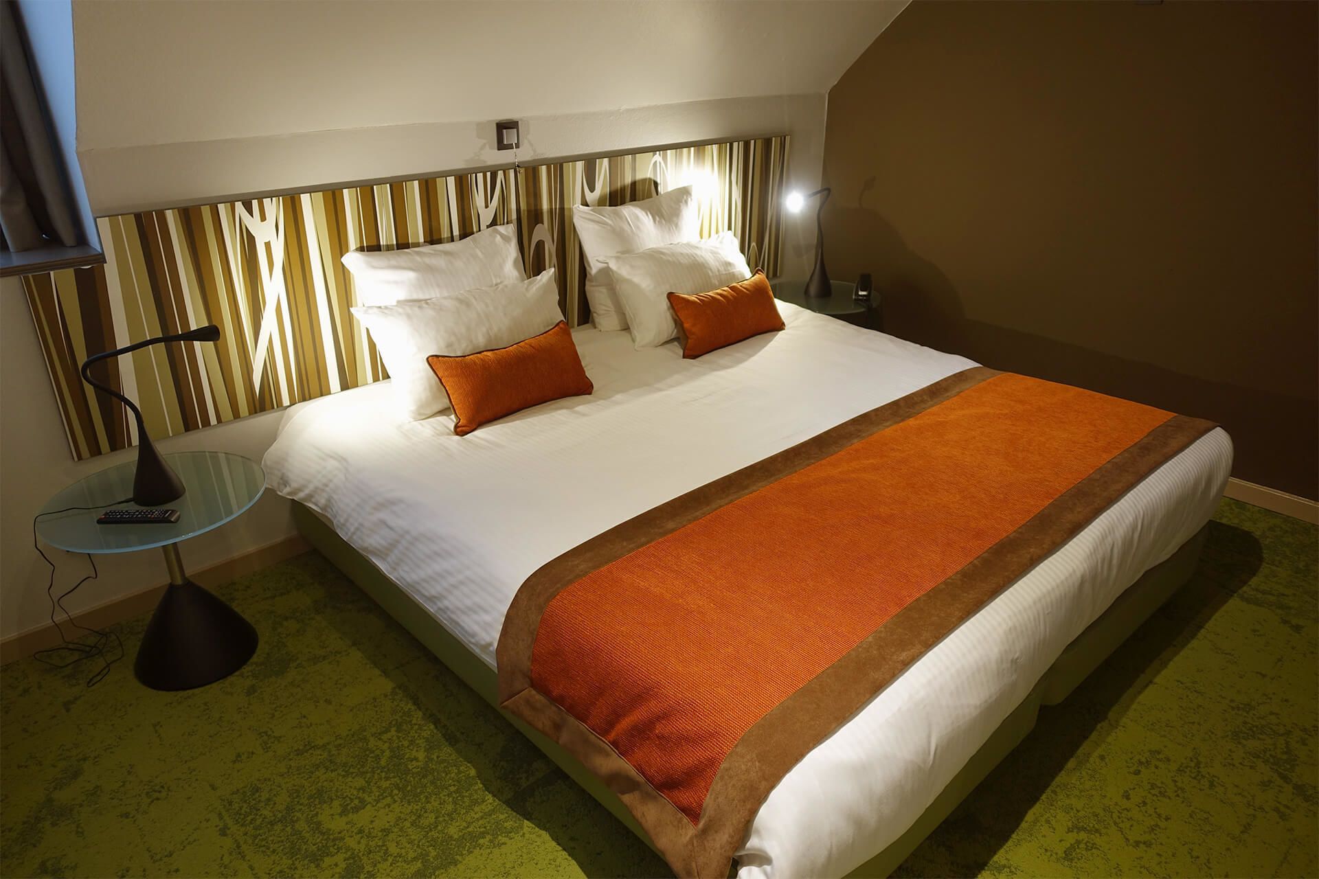 A hotel room with a large bed, a glass side table, and a modern headboard.