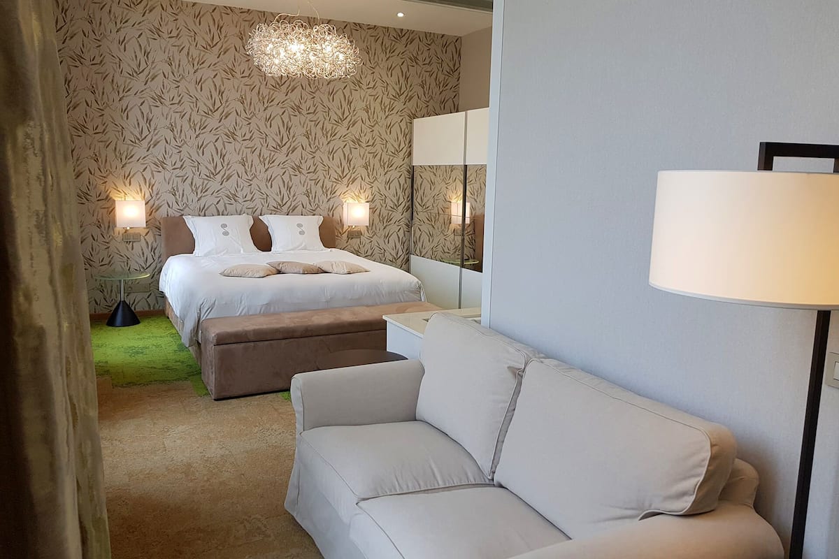 A hotel room with a bed, a sofa, a mirror, and two bedside lamps.