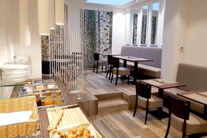 Un comedor moderno con un bufé, disposición de mesas y sillas, y una vista a través de una pared decorativa.