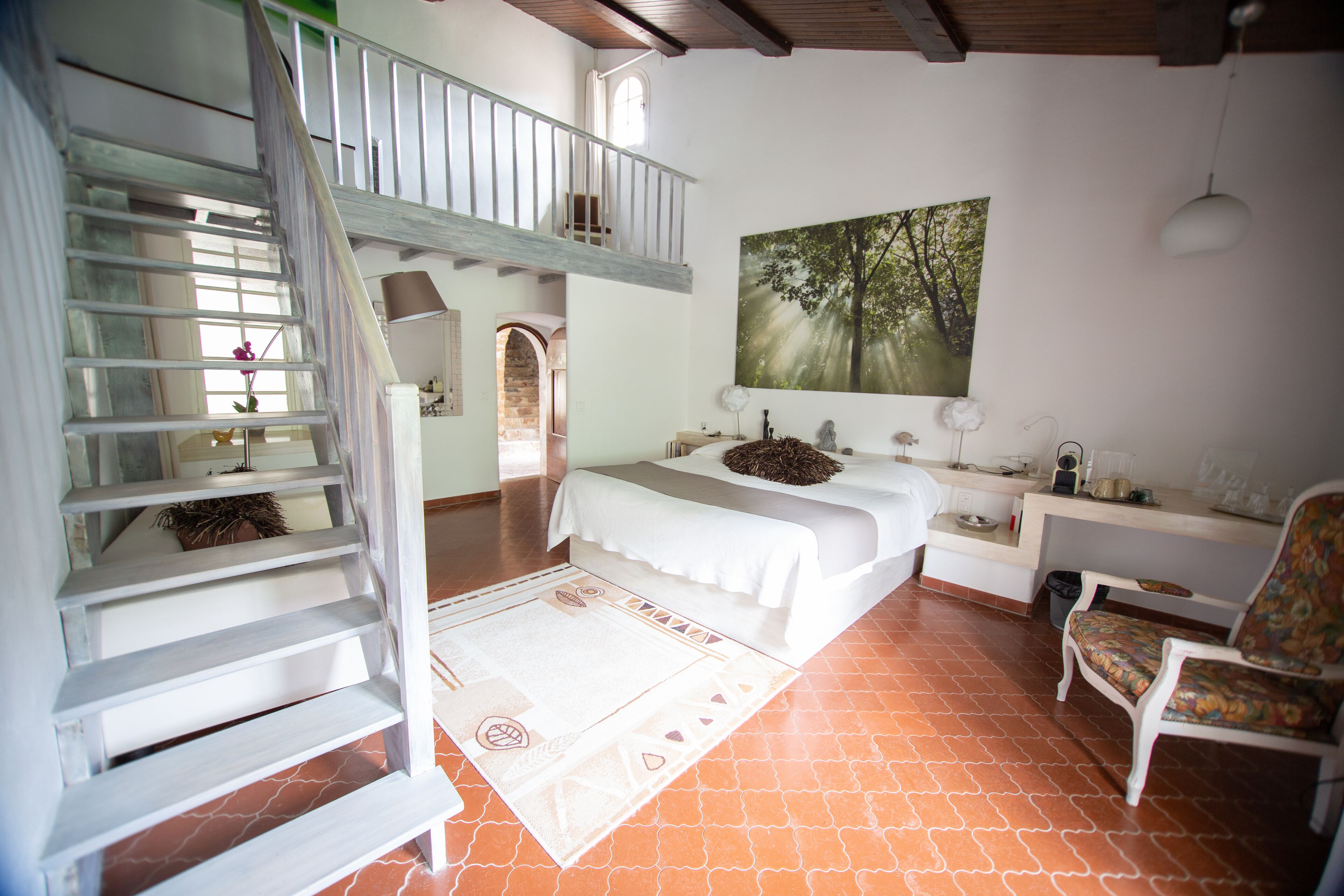 Un dormitorio con cama, una silla, un escritorio, una escalera y un cuadro de un bosque.