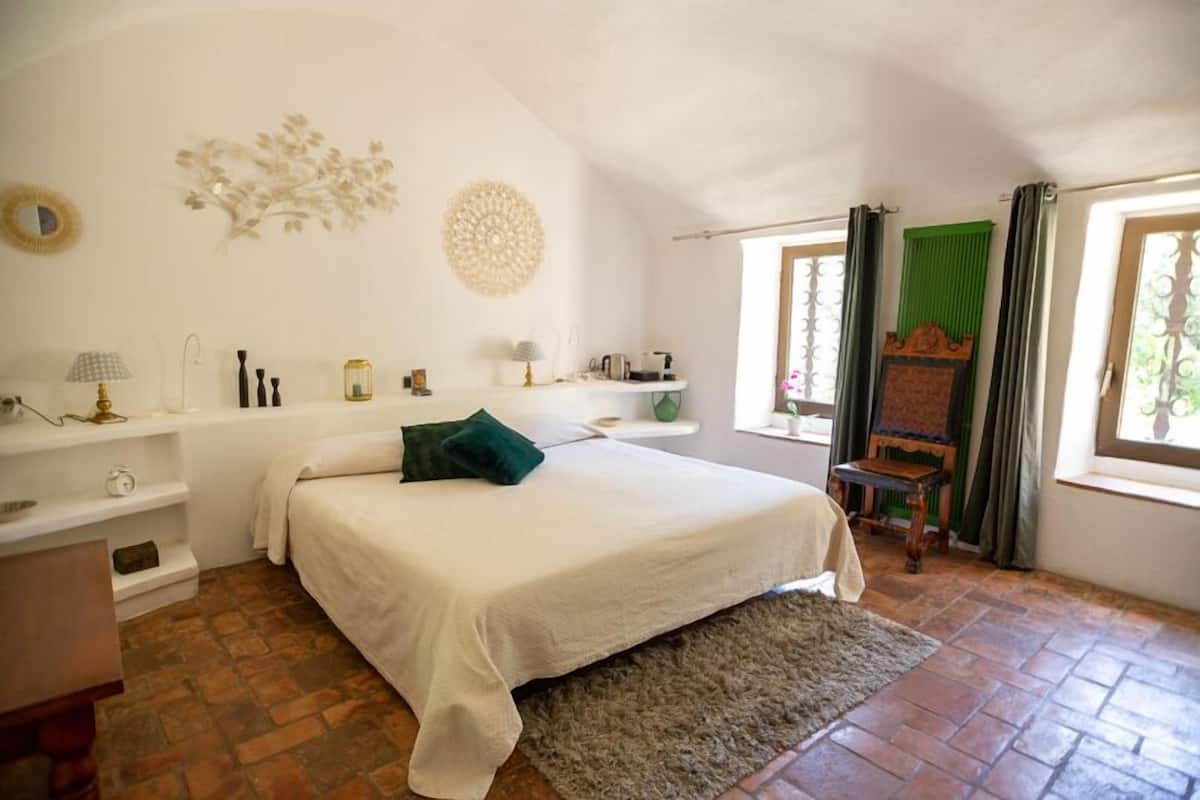 A bedroom with a bed, a nightstand, a dresser, a window with curtains, and a decorative wall piece.