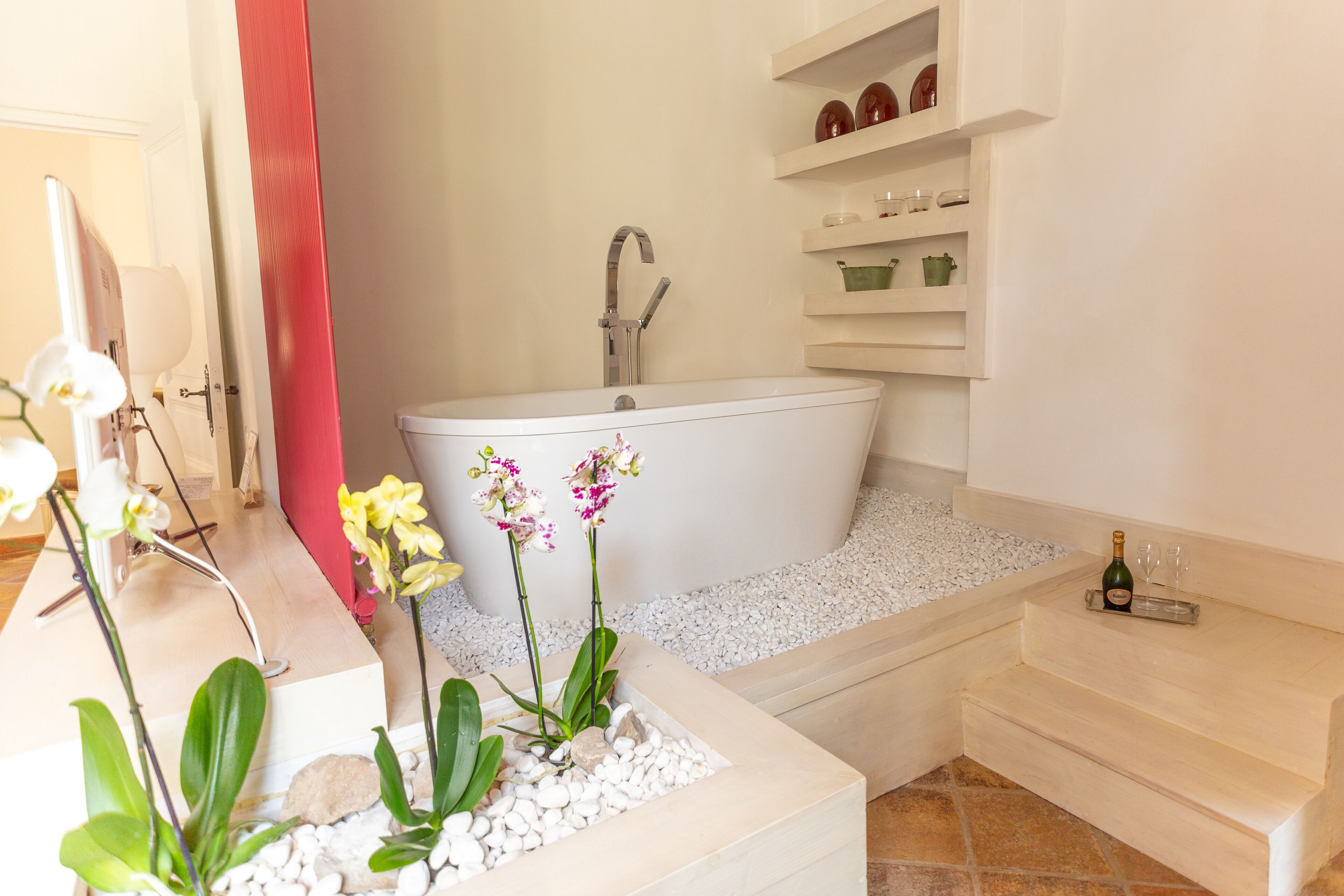 Une salle de bain moderne avec une baignoire sur pieds, des étagères blanches ornées d’objets décoratifs et un petit marchepied menant à la baignoire.