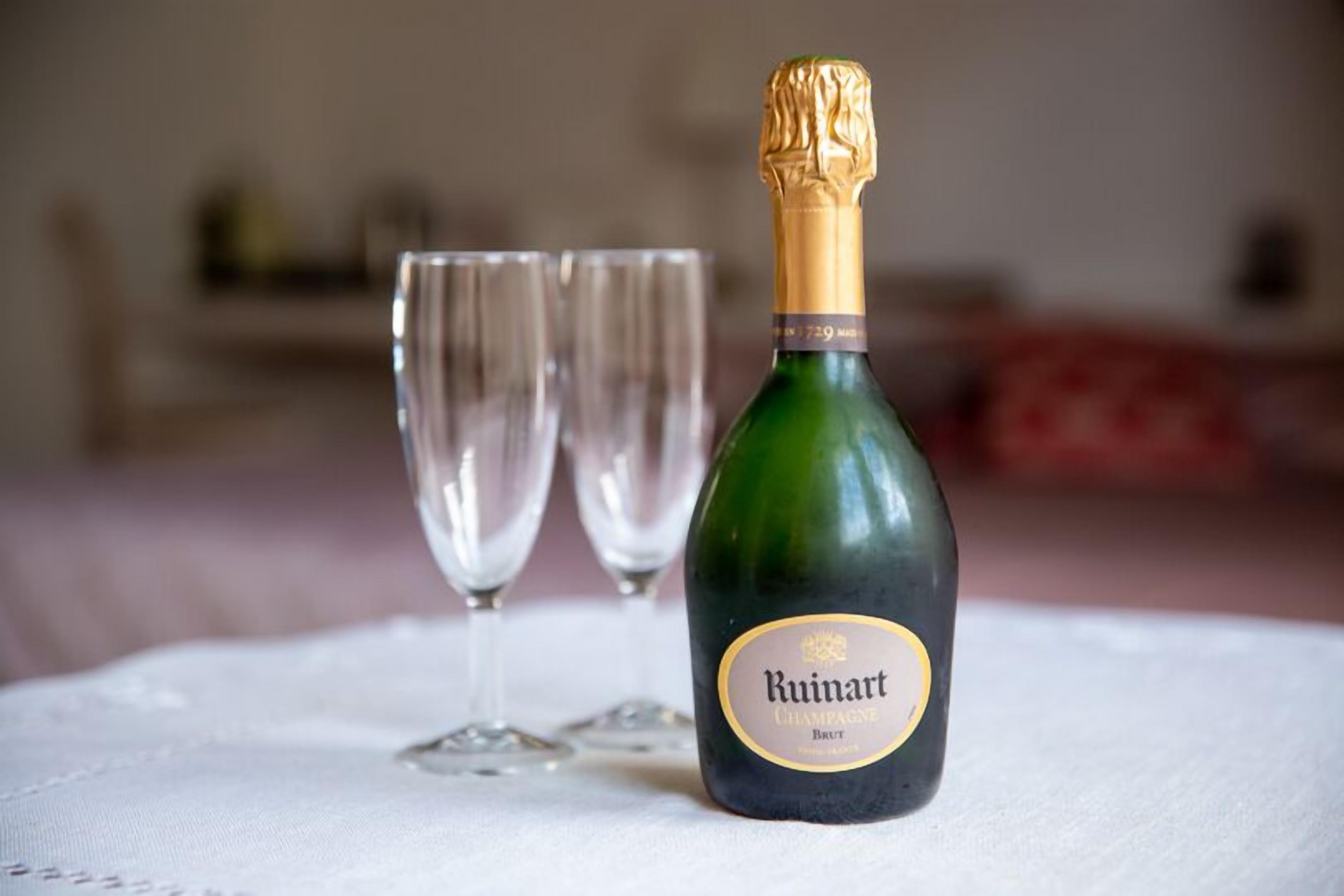A Ruinart champagne bottle on a white tablecloth with two empty glasses.