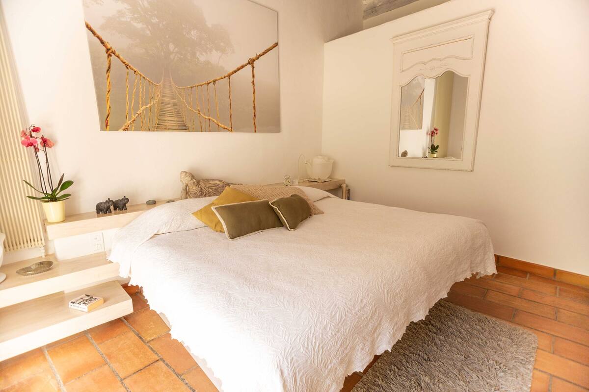 A bedroom with a bed, a nightstand, a mirror, and a painting of a bridge.