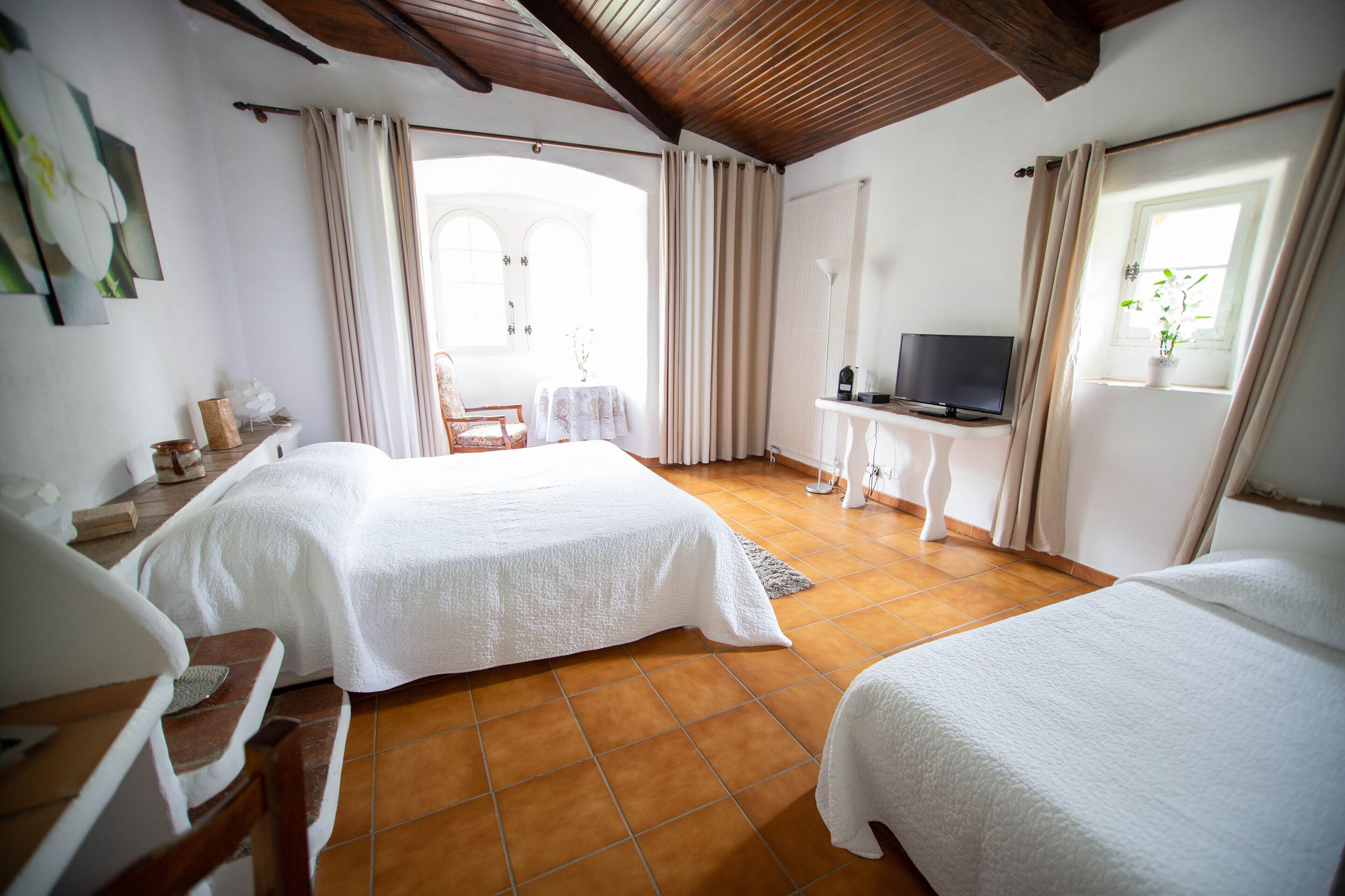 A bedroom with two beds, a TV, and a window with curtains.