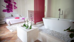 Un baño moderno con una bañera blanca, un lavamanos blanco y una pequeña maceta blanca con orquídeas.