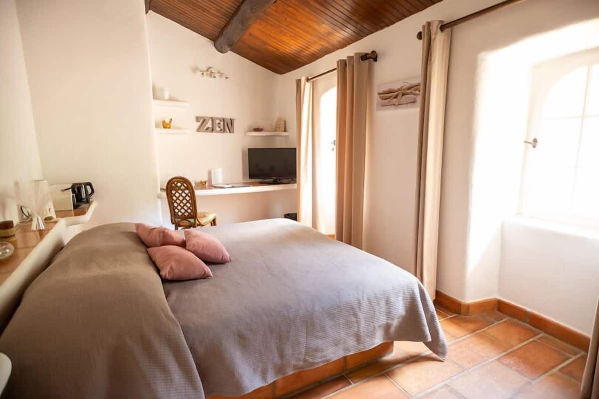 A bedroom with a bed, a TV, a chair, and a window with curtains.