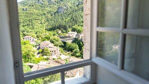 Vista a través de una ventana de un pueblo con edificios rodeados de vegetación y montañas.
