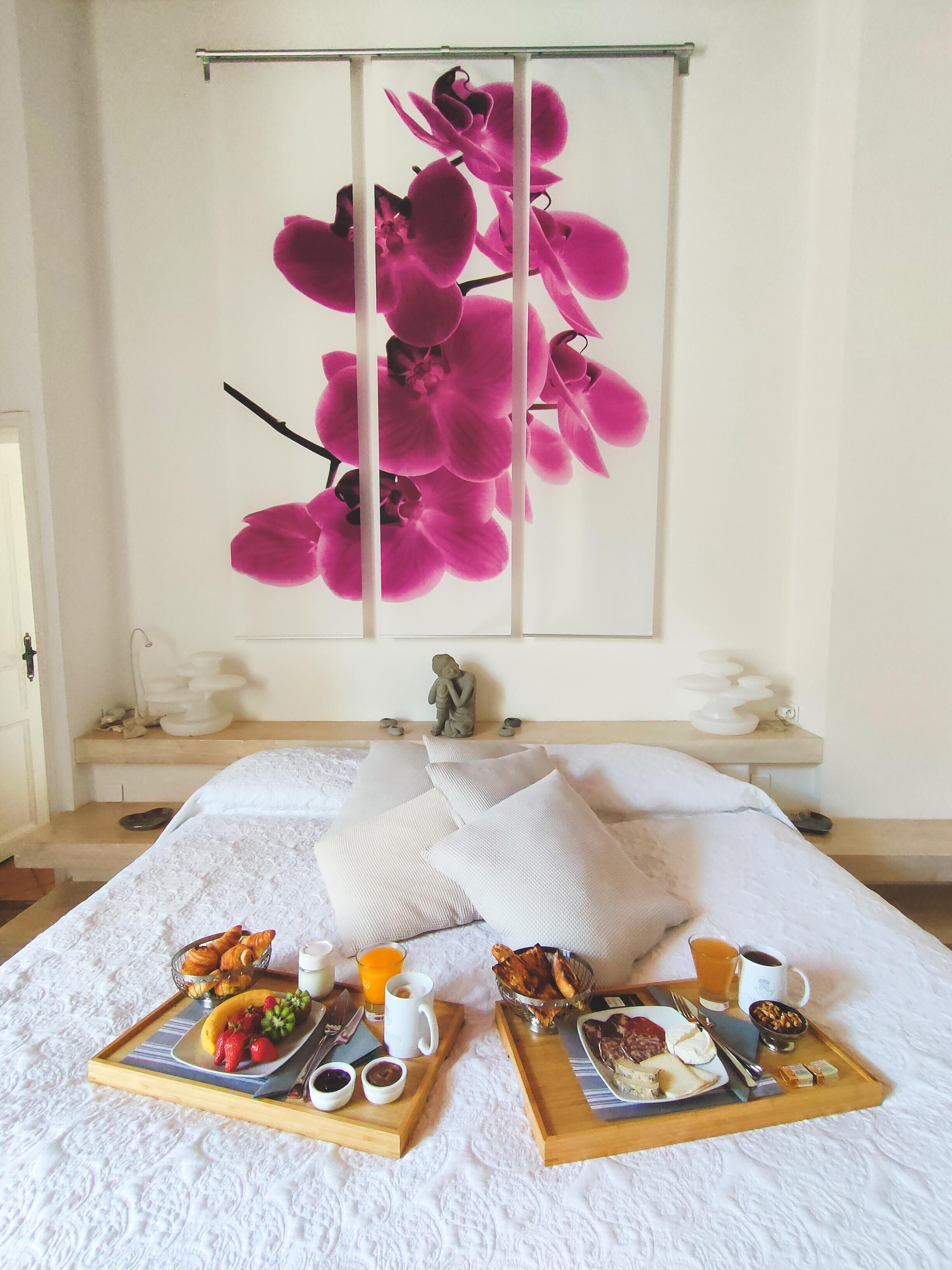 Una cama impecablemente arreglada con una bandeja de desayuno, una estatua y un cuadro grande de orquídeas en la pared.