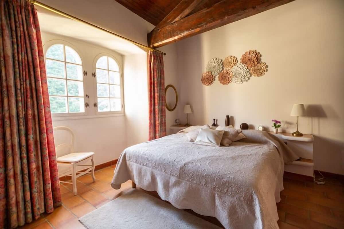 A bedroom with a large bed, a chair, a bedside table with lamps, and a wall decoration.