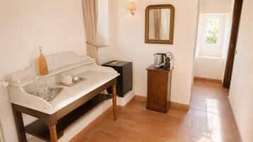 A room with a marble countertop, a bottle, glasses, a kettle, a coffee maker, a mirror, and a door leading to another room.