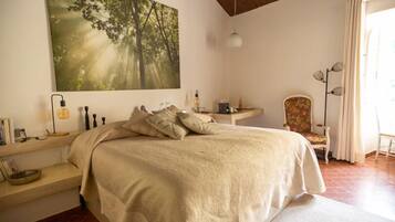 A bedroom with a large bed, a bedside table, a chair, and a painting of a forest.
