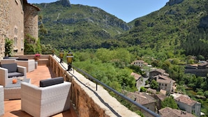Una terraza con mobiliario de mimbre y un muro de piedra con vistas a un pueblo y montañas.