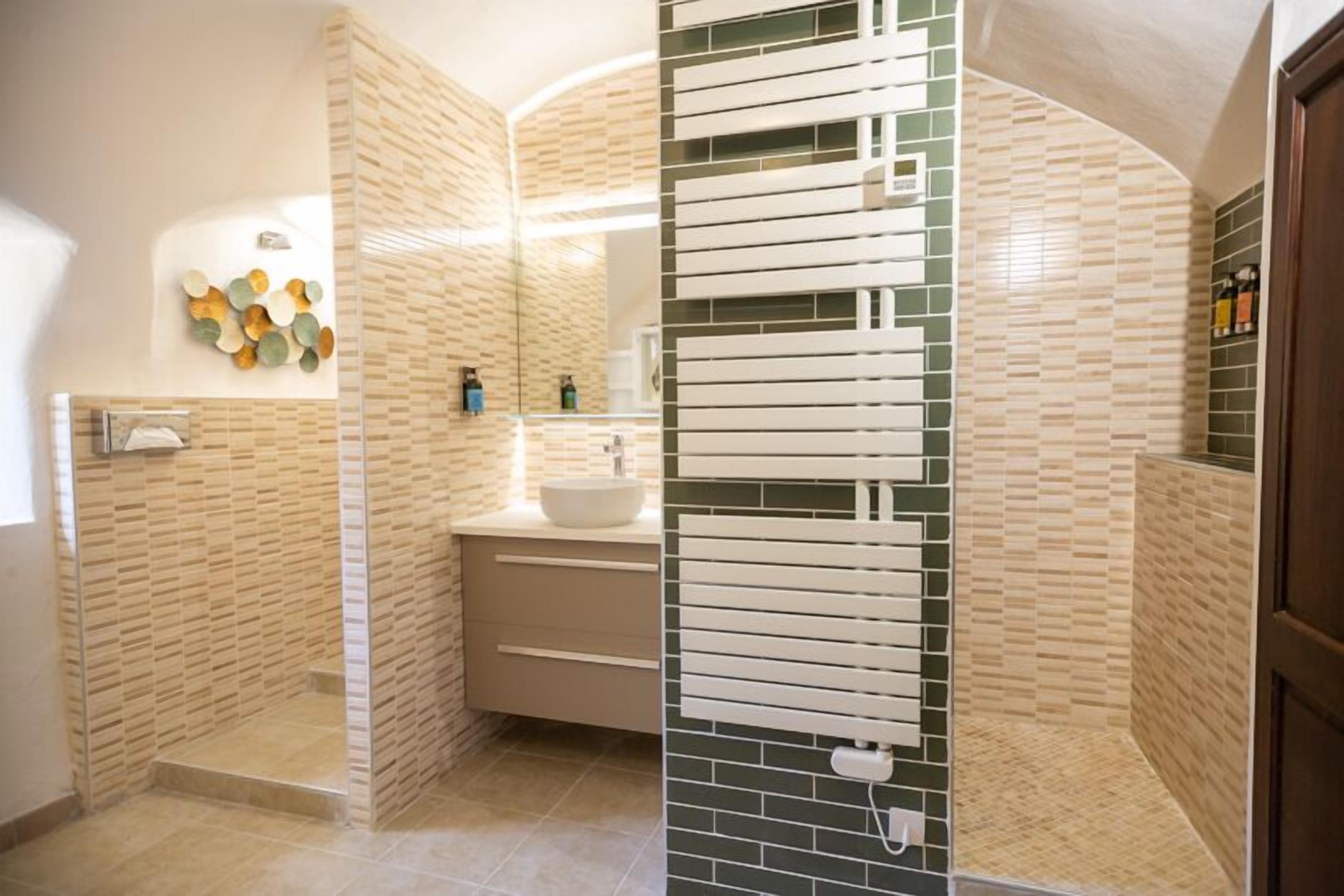 A modern bathroom with a glass-enclosed shower, a white sink, and a mirror with a green-tiled backsplash.