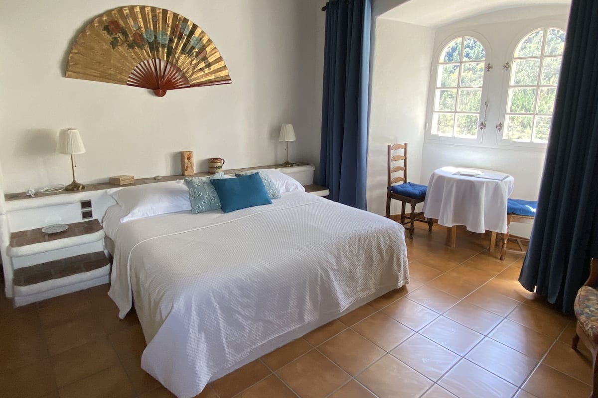 A bedroom with a bed, bedside tables, a chair, a table, and a window with curtains.