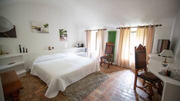 Un dormitorio con una cama grande, una silla de madera, un escritorio con una lámpara y una cortina verde.