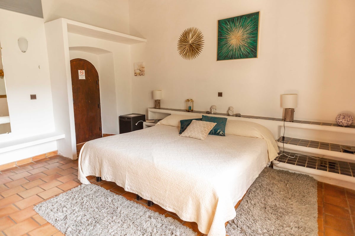 A bedroom with a large bed, a nightstand, a dresser, and a wall-mounted heater.
