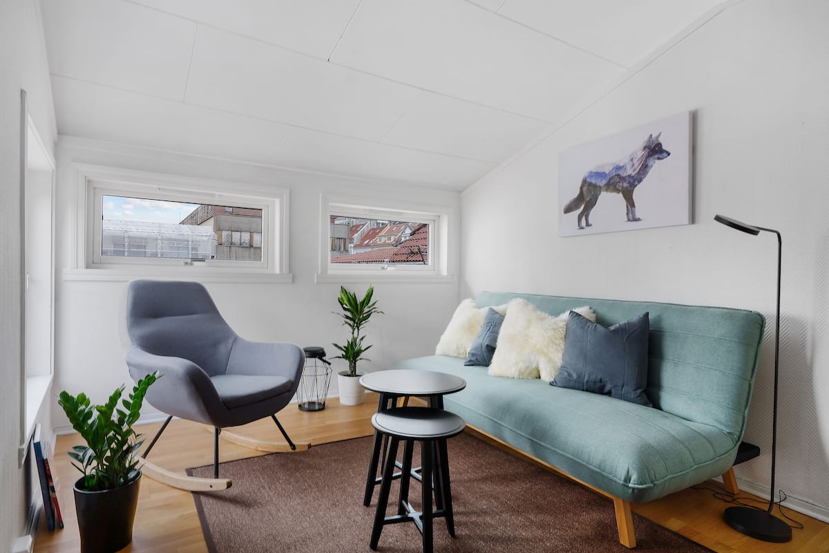 A modern living room with a teal sofa, a grey armchair, a round table, and a potted plant.