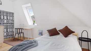 A bedroom with a bed, a desk, a chair, a small table, and a window.