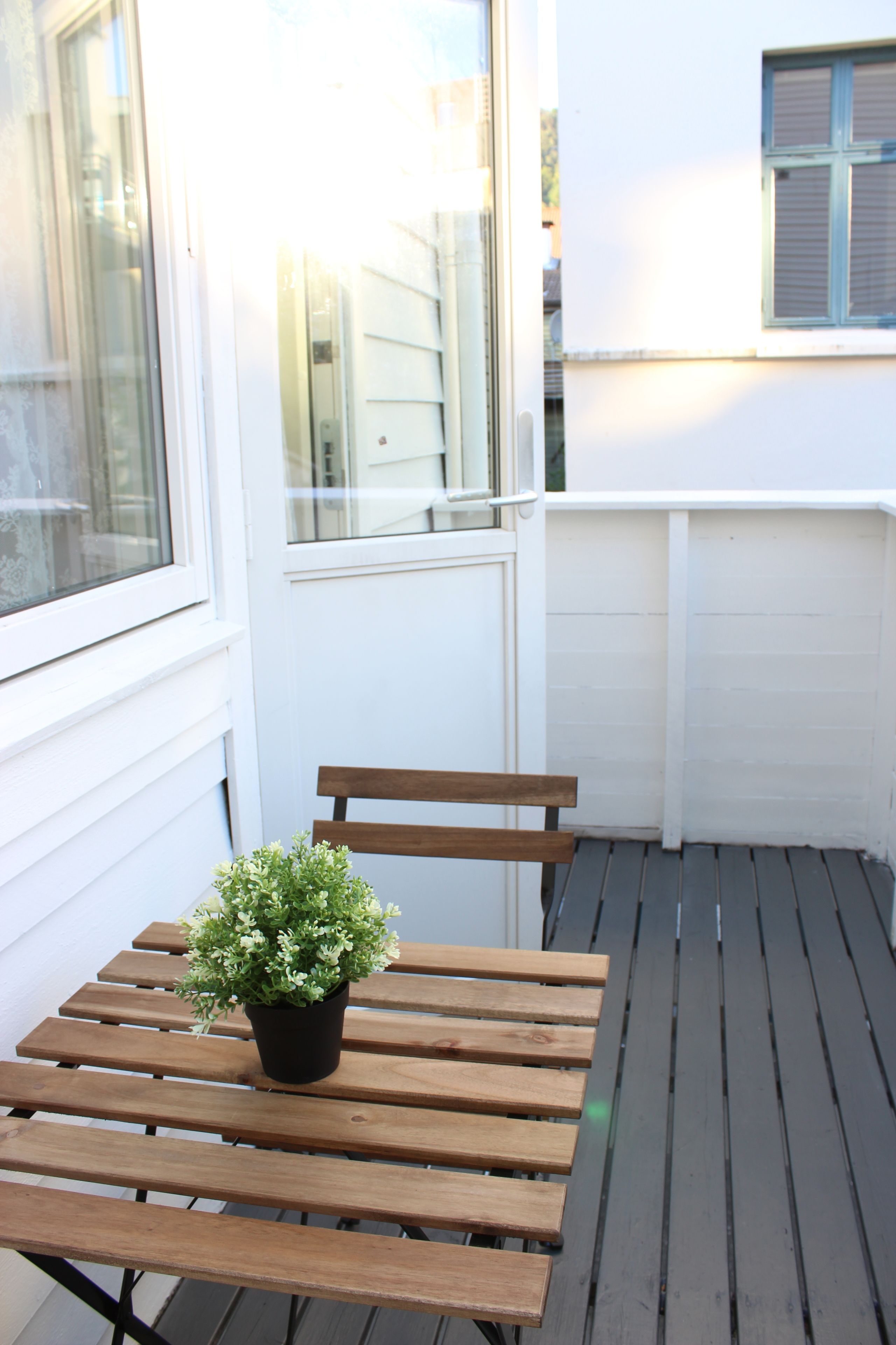 A wooden bench with a potted plant on a balcony with white walls and windows.